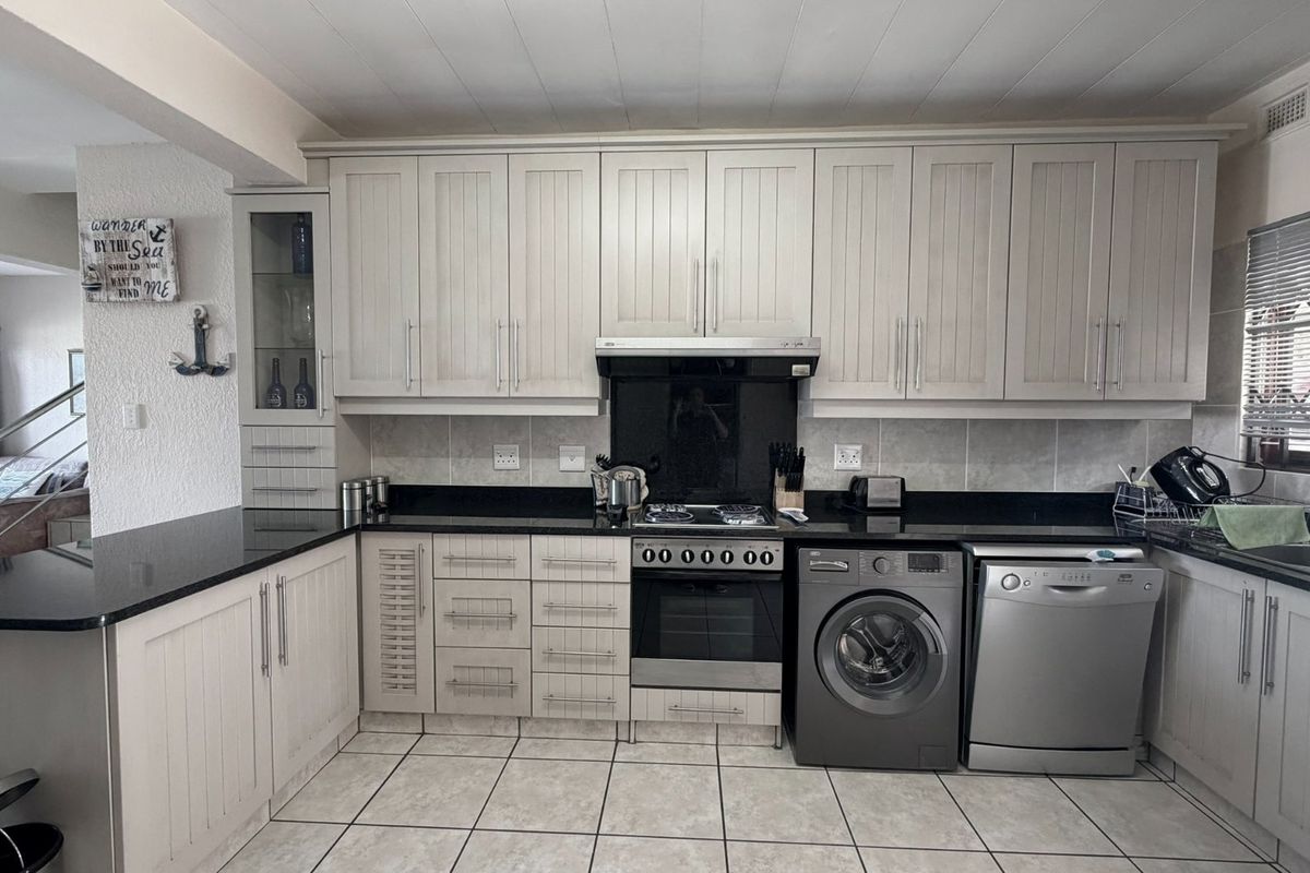 A functional kitchen featuring light-toned cabinetry, granite countertops, a gas hob with extractor, and integrated space for laundry and dishwashing appliances.