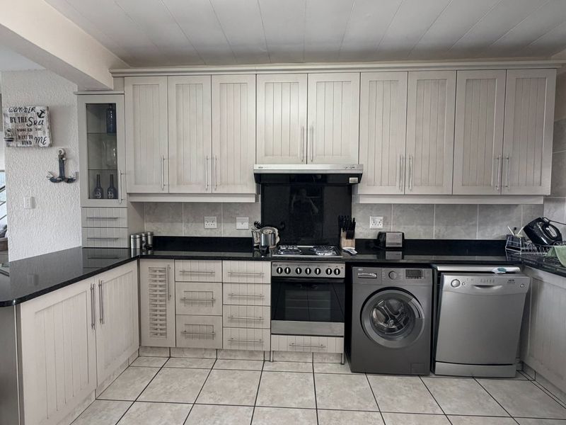 A functional kitchen featuring light-toned cabinetry, granite countertops, a gas hob with extractor, and integrated space for laundry and dishwashing appliances.