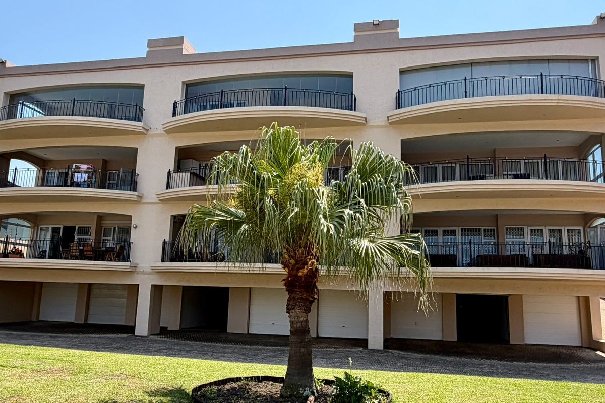 Rear view of a multi-story apartment complex featuring private balconies with wrought iron railings and ground-level garage access.