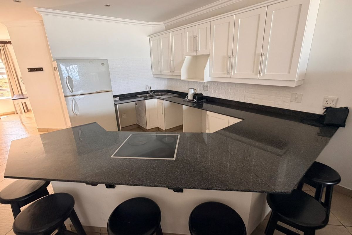 A functional kitchen featuring dark granite countertops, white cabinetry, an integrated electric hob, and a tiled backsplash, offering a clean and practical workspace.