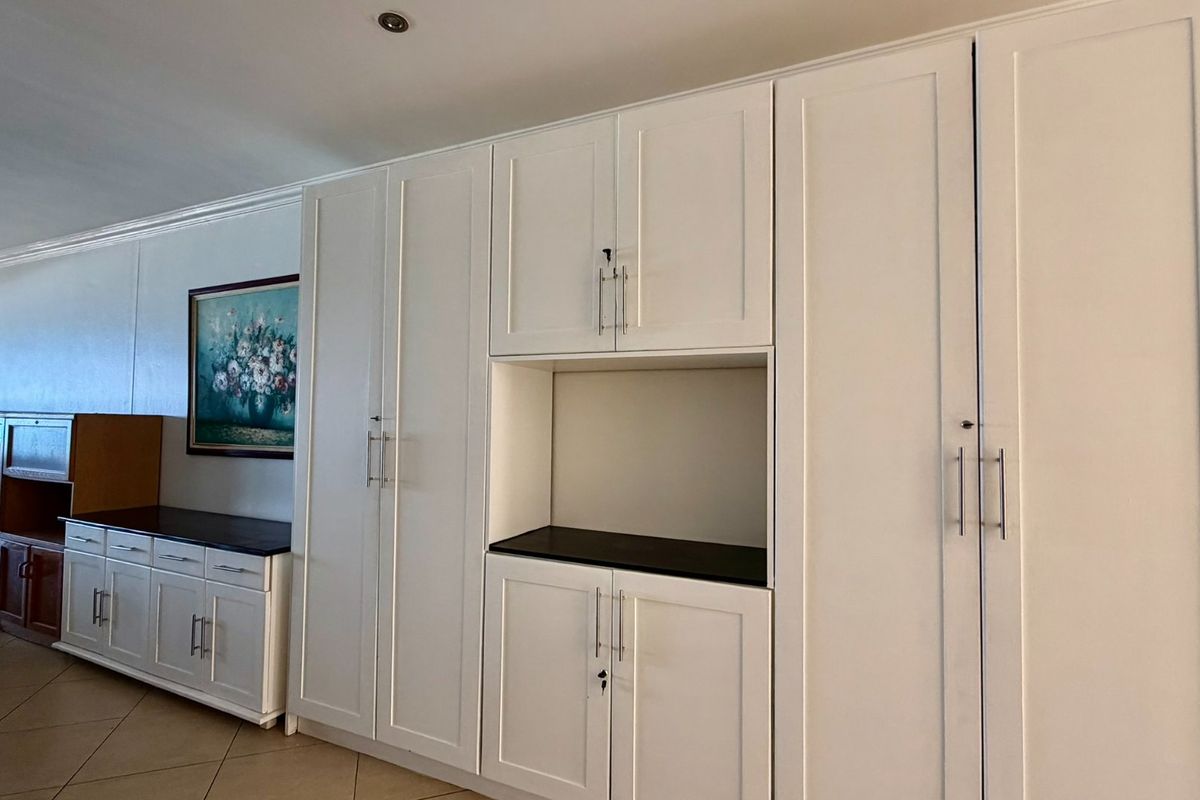 A living area featuring extensive white built-in cabinetry with dark countertops, recessed ceiling lighting, and tiled flooring.