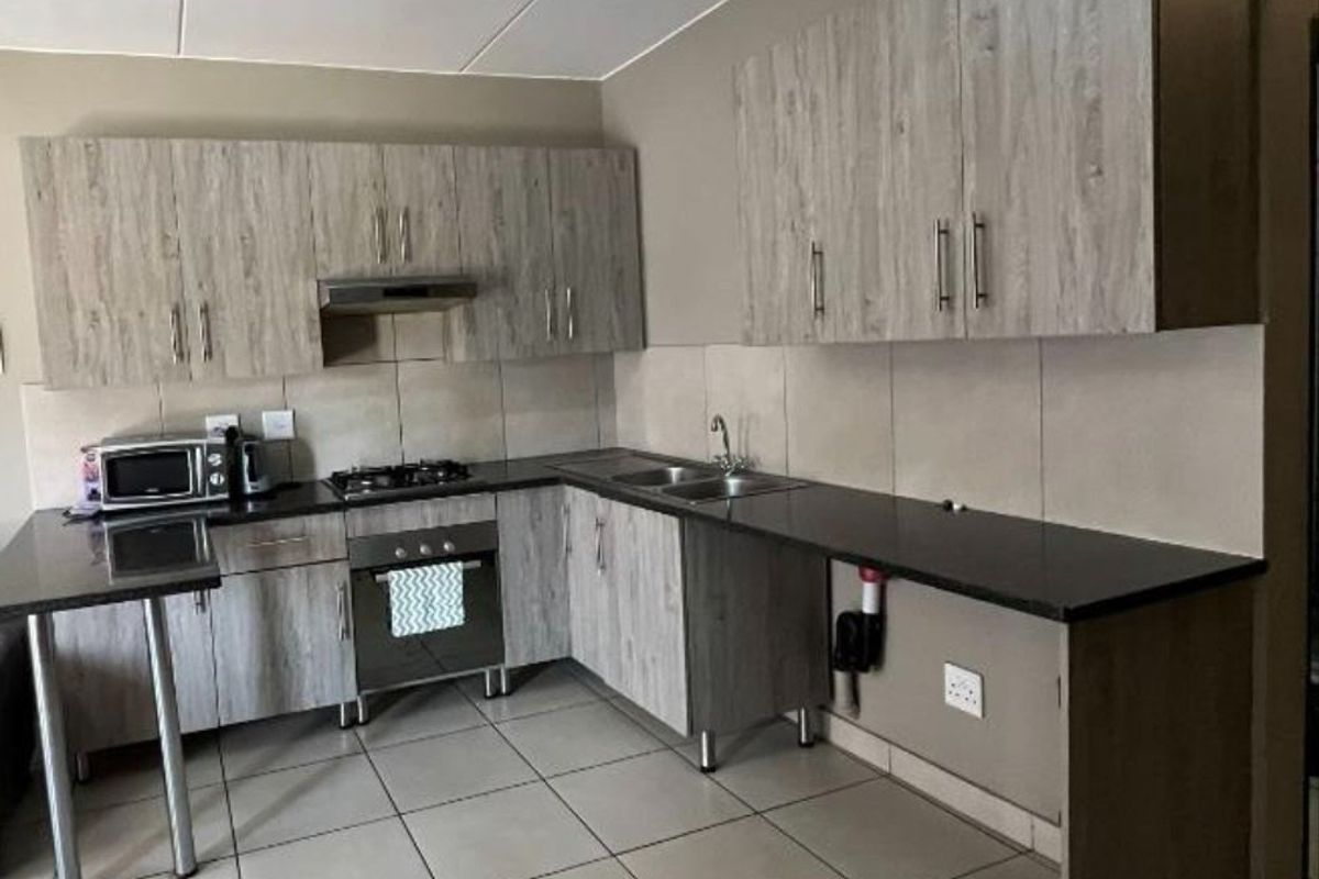 A functional kitchen featuring wood-look cabinetry, dark countertops, a built-in oven with gas hob, and tiled flooring throughout.
