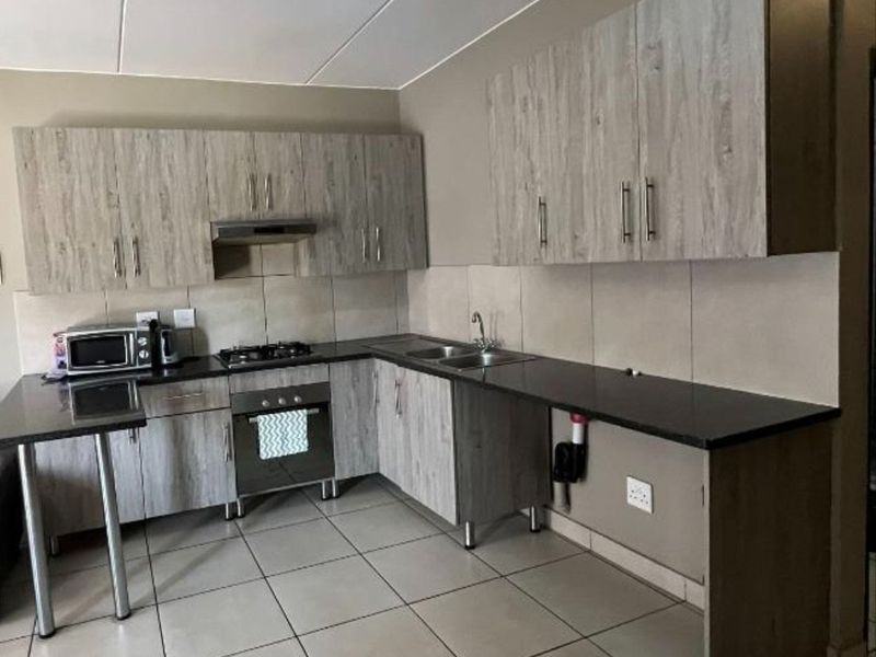 A functional kitchen featuring wood-look cabinetry, dark countertops, a built-in oven with gas hob, and tiled flooring throughout.