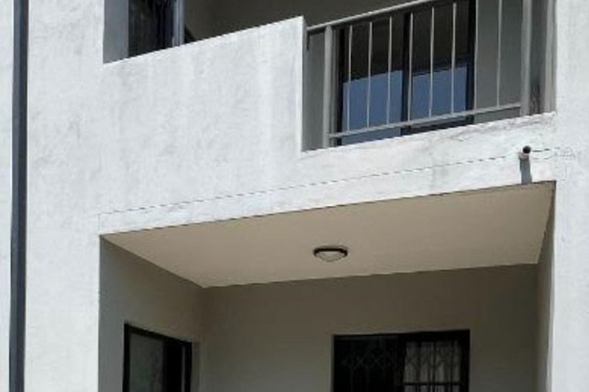 A view of the rear exterior featuring a ground-floor tiled patio, a first-floor balcony with metal railing, and sliding door access.