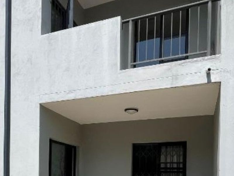 A view of the rear exterior featuring a ground-floor tiled patio, a first-floor balcony with metal railing, and sliding door access.