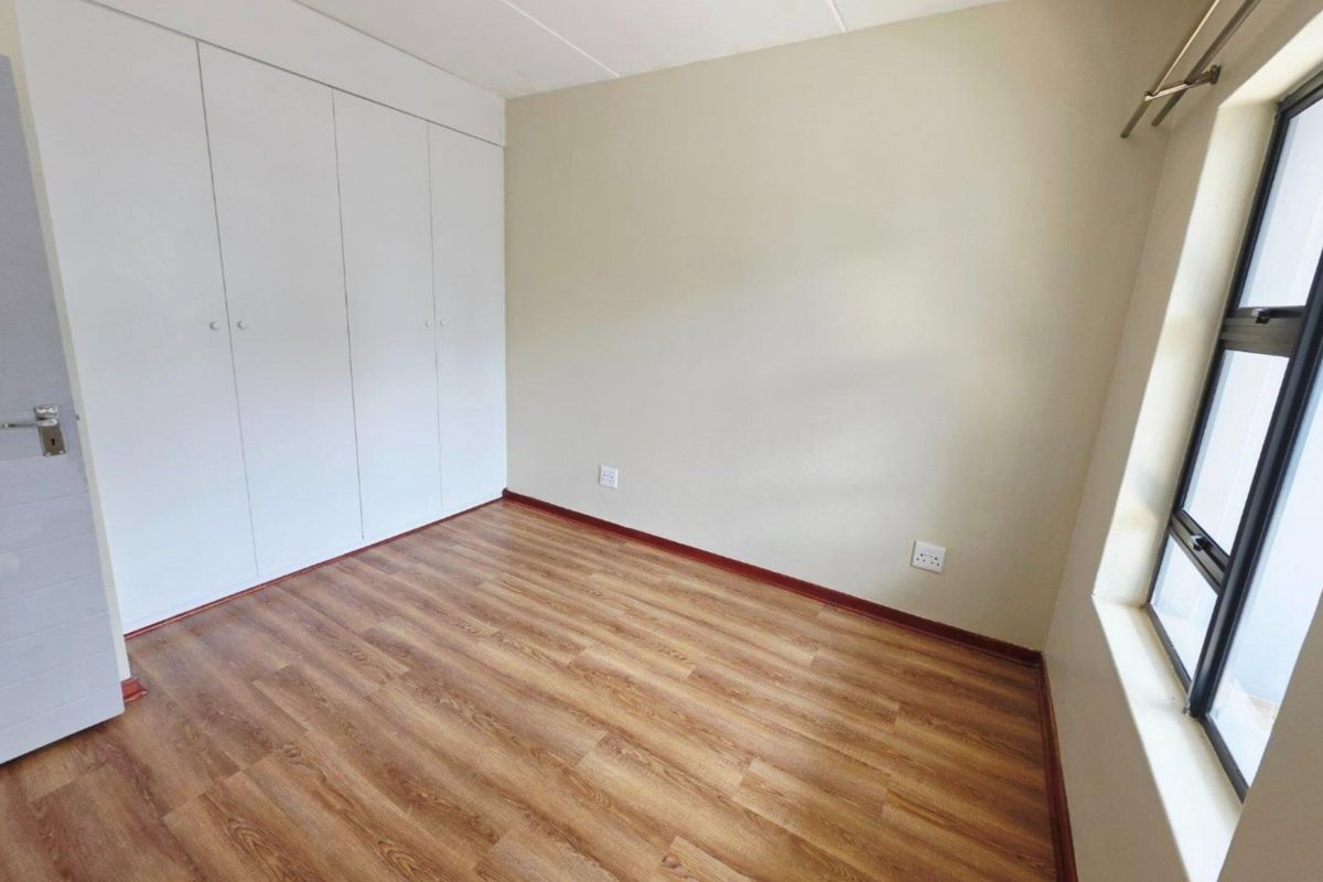 A bright, empty bedroom featuring modern laminate flooring, neutral wall tones, and ample built-in cupboard storage space.
