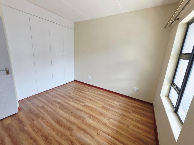 A bright, empty bedroom featuring modern laminate flooring, neutral wall tones, and ample built-in cupboard storage space.
