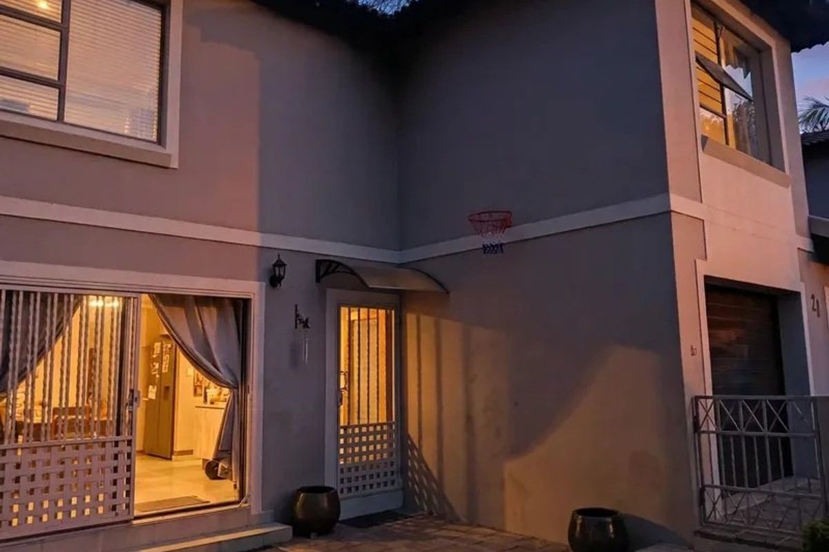 Rear exterior view of the townhouse featuring a paved patio area, sliding glass doors, and secure access points at dusk.