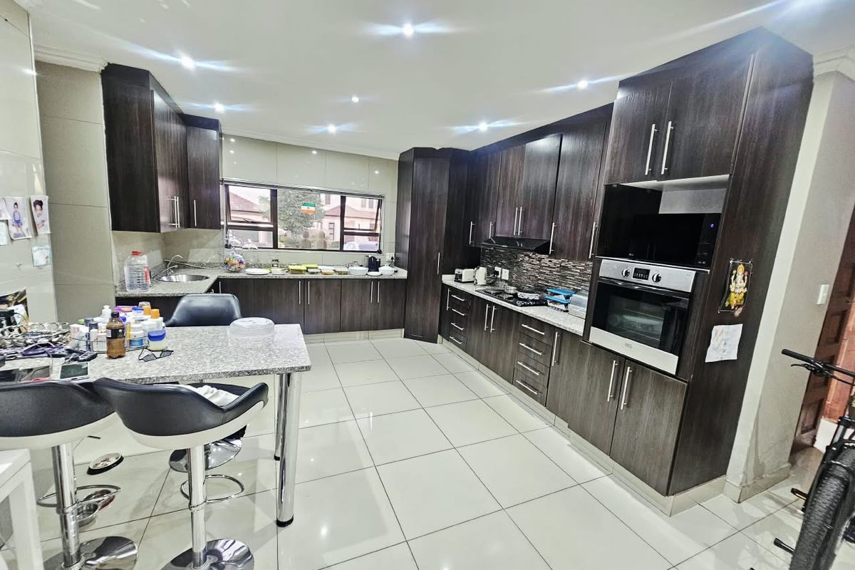 Modern kitchen featuring dark wood cabinetry, granite countertops, built-in oven, hob, extractor fan, and tiled flooring with recessed lighting.