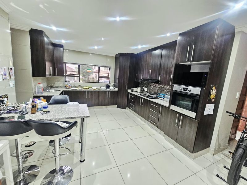 Modern kitchen featuring dark wood cabinetry, granite countertops, built-in oven, hob, extractor fan, and tiled flooring with recessed lighting.