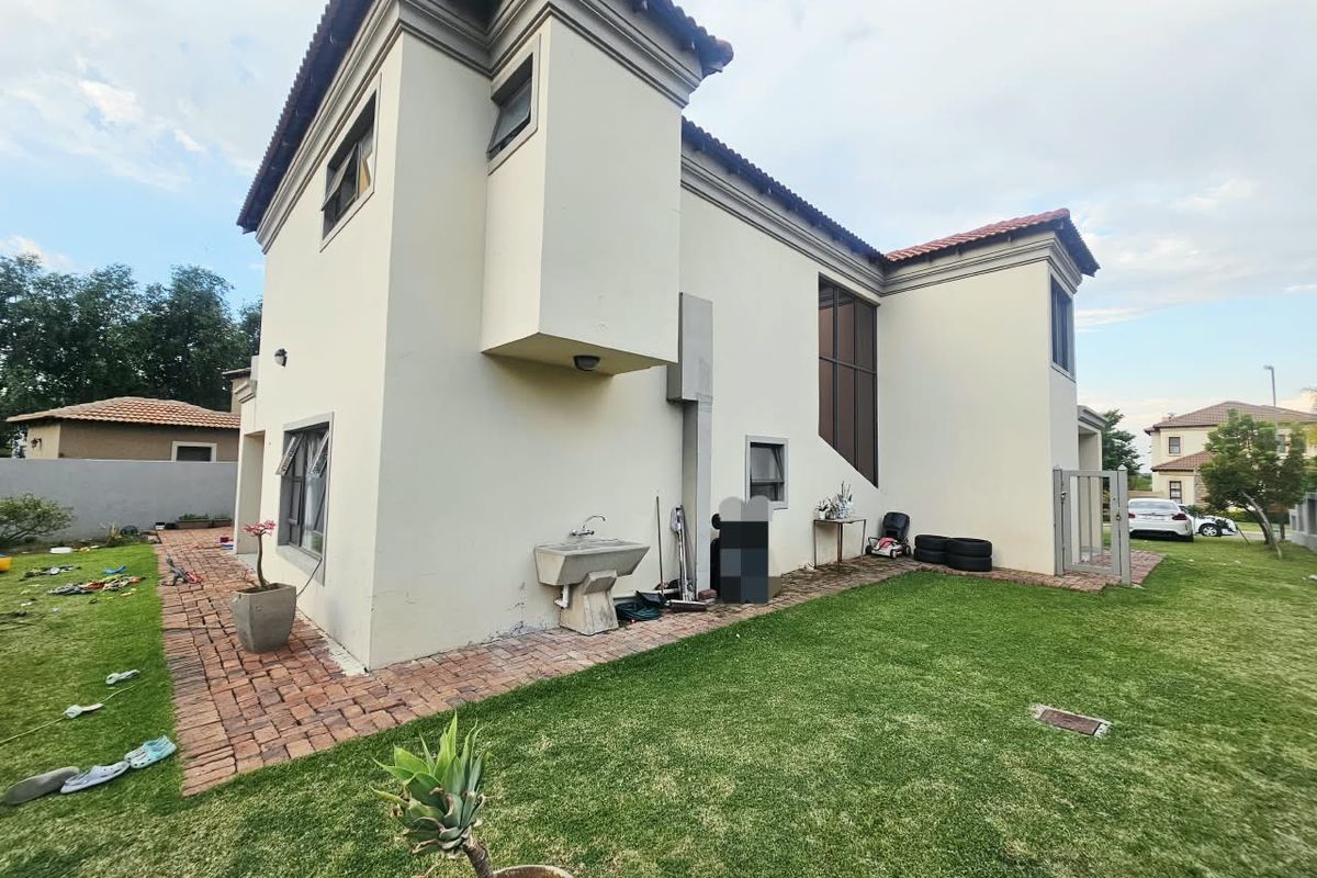 Rear view of the double-story house featuring a brick paved walkway, landscaped lawn, and an external utility sink attached to the exterior wall.