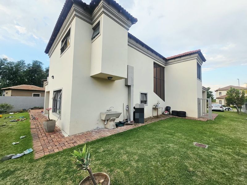 Rear view of the double-story house featuring a brick paved walkway, landscaped lawn, and an external utility sink attached to the exterior wall.