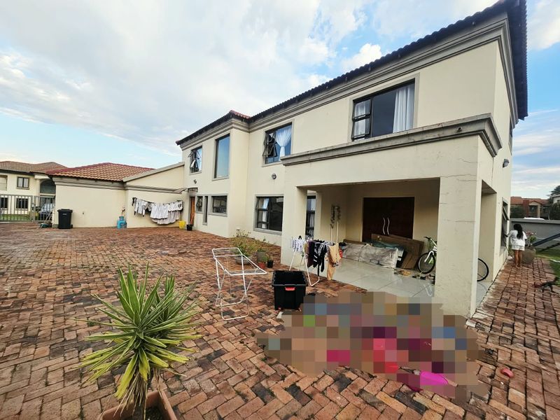 Rear view of the property featuring a large brick-paved courtyard and a covered patio area with tiled flooring.