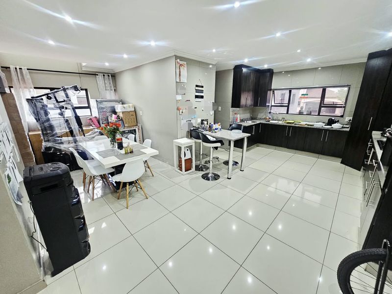 Spacious open-plan kitchen and dining area featuring dark wood cabinetry, granite countertops, modern tiled flooring, and recessed downlighting throughout.