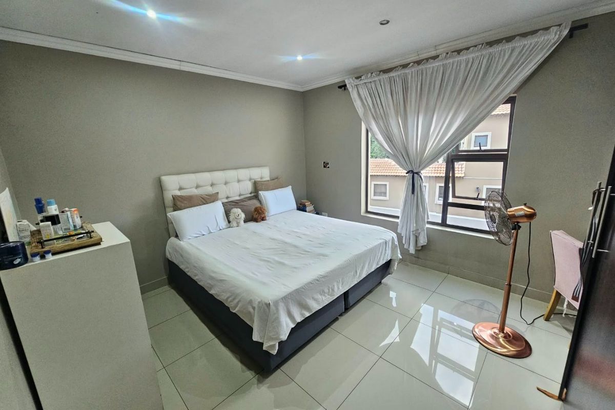 A well-maintained bedroom featuring neutral wall tones, large format floor tiles, and recessed downlighting, offering a clean and functional living space.