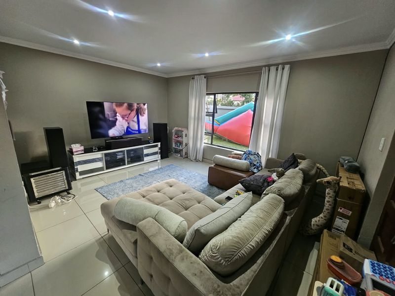 A comfortable living room featuring tiled flooring, recessed downlighting, and large windows that provide natural light and a view of the garden.