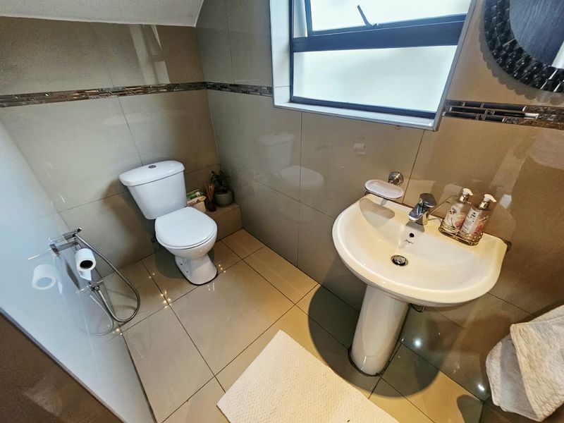 A modern, well-maintained bathroom featuring tiled walls and flooring, a pedestal basin with a chrome mixer tap, and a standard toilet.