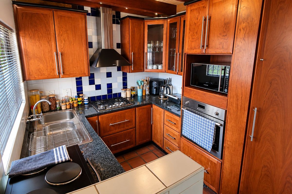A functional kitchen featuring warm wooden cabinetry, granite countertops, a gas hob, built-in oven, and a tiled backsplash.