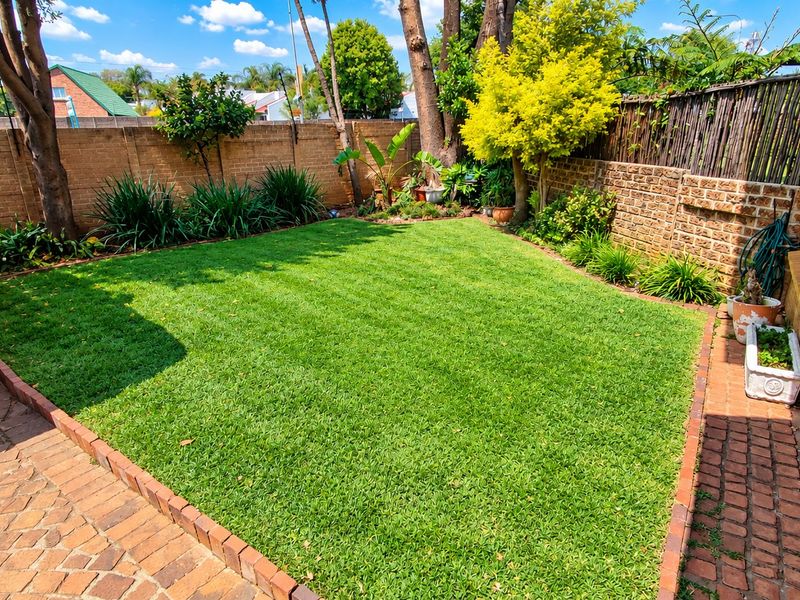 A well-maintained rear garden featuring a manicured lawn, brick paving, and a perimeter brick boundary wall.