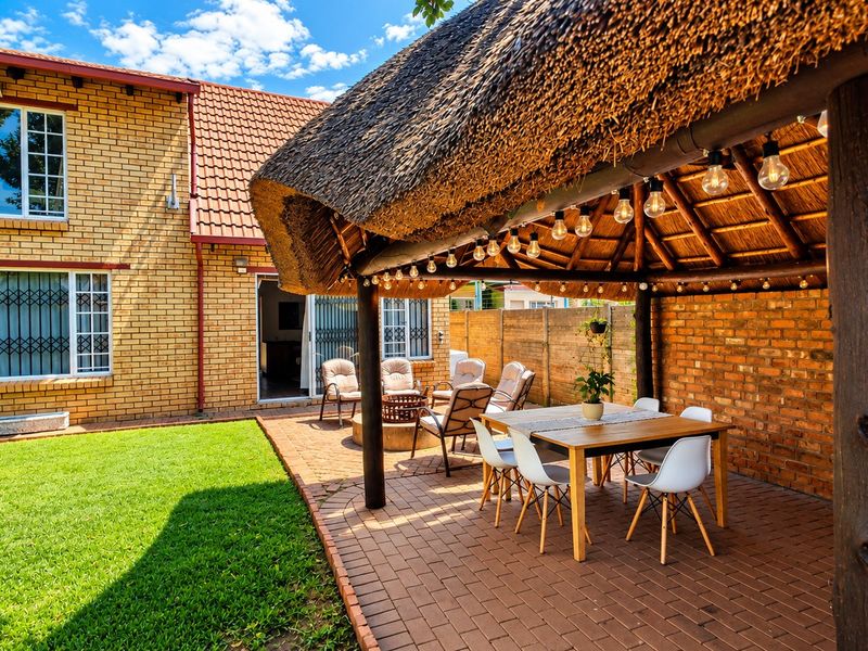 A spacious outdoor patio area featuring a traditional thatched roof, brick paving, and a well-maintained lawn, perfect for outdoor dining and relaxation.