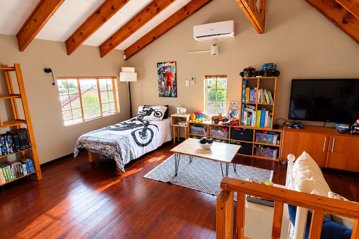 Spacious loft-style bedroom featuring exposed timber rafters, hardwood flooring, and a split-system air conditioner, offering a warm and inviting atmosphere.