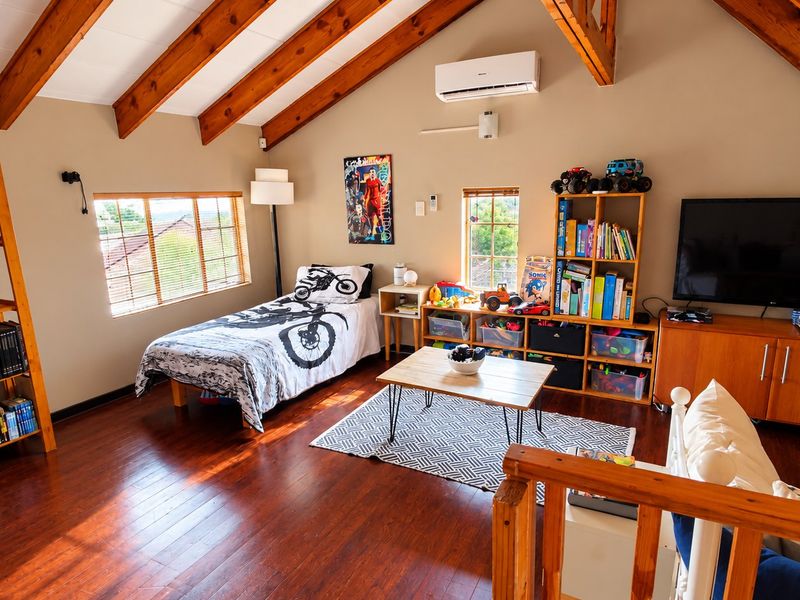 Spacious loft-style bedroom featuring exposed timber rafters, hardwood flooring, and a split-system air conditioner, offering a warm and inviting atmosphere.