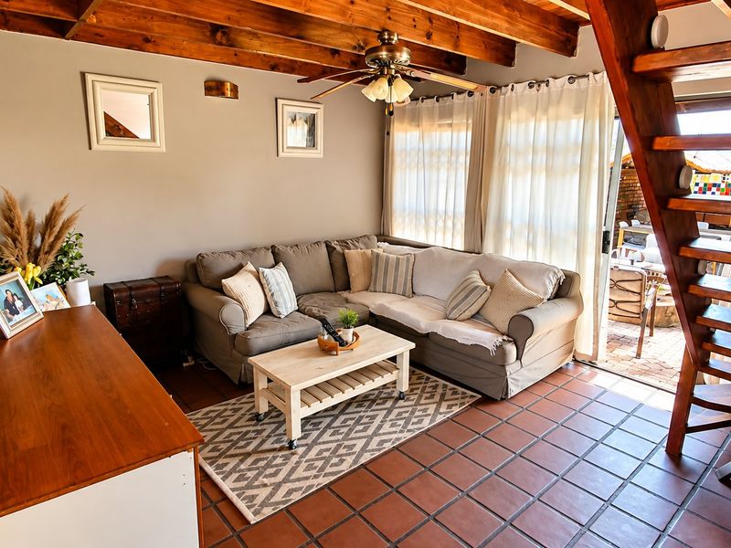 Cozy living room featuring exposed timber ceiling beams, terracotta floor tiles, and a wooden staircase leading to an upper level, with direct patio access.
