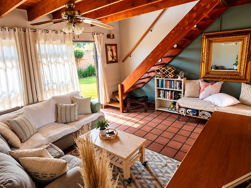 Spacious living room featuring exposed timber ceiling beams, a wooden staircase, and terracotta floor tiles, with direct access to the garden through sliding doors.
