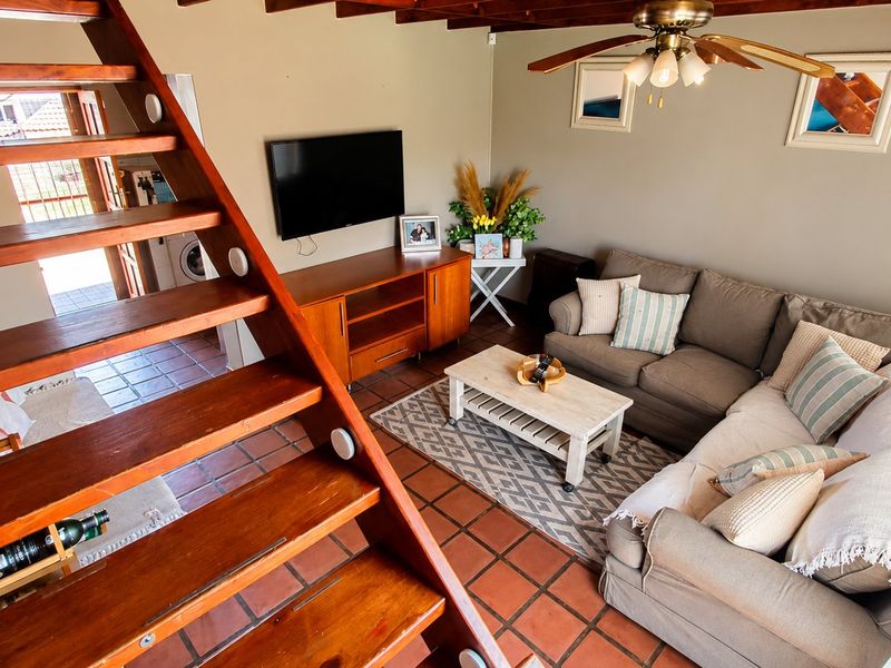 Cozy living room featuring exposed timber ceiling beams, a wooden staircase, and terracotta floor tiles, creating a warm and inviting atmosphere.