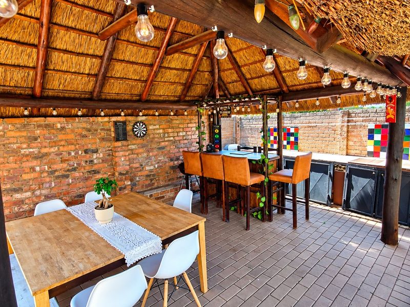 Covered outdoor entertainment area featuring a rustic thatched roof, exposed brick walls, and a built-in bar counter, perfect for alfresco dining and social gatherings.