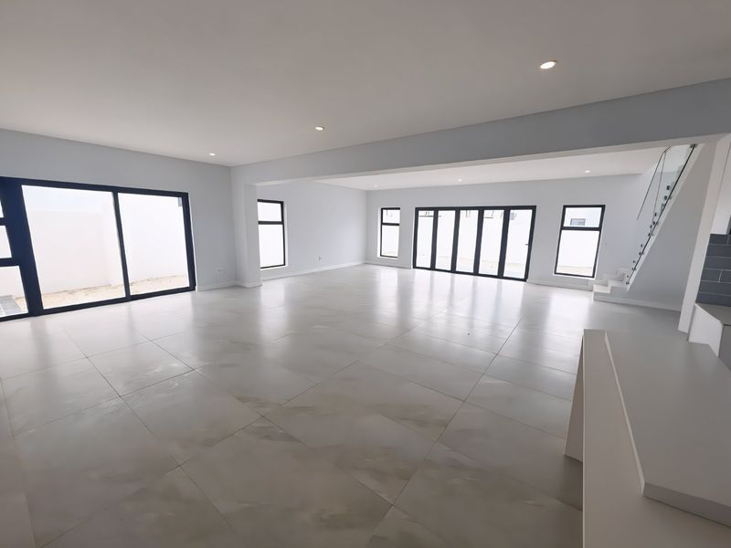 Spacious open-plan living area featuring large format floor tiles, modern recessed lighting, and extensive glass doors providing abundant natural light and seamless outdoor access.