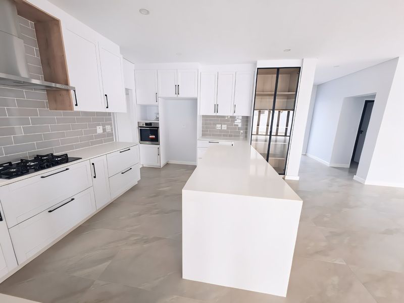 Modern, newly renovated kitchen featuring a large central island, white shaker cabinetry, stone countertops, built-in oven, gas hob, and a stylish glass-fronted pantry.