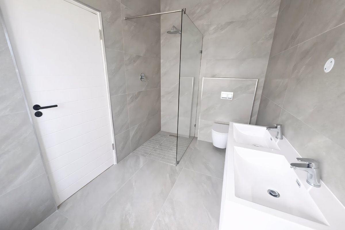Modern bathroom featuring a walk-in shower with glass screen, wall-hung toilet, and a sleek dual vanity basin with contemporary chrome fixtures.