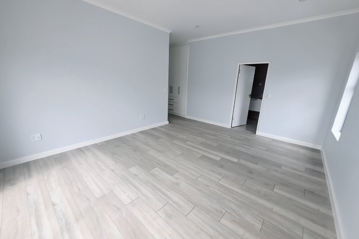 A bright, modern bedroom featuring light grey laminate flooring, neutral walls, built-in cupboards, and recessed lighting, offering a clean and spacious living environment.