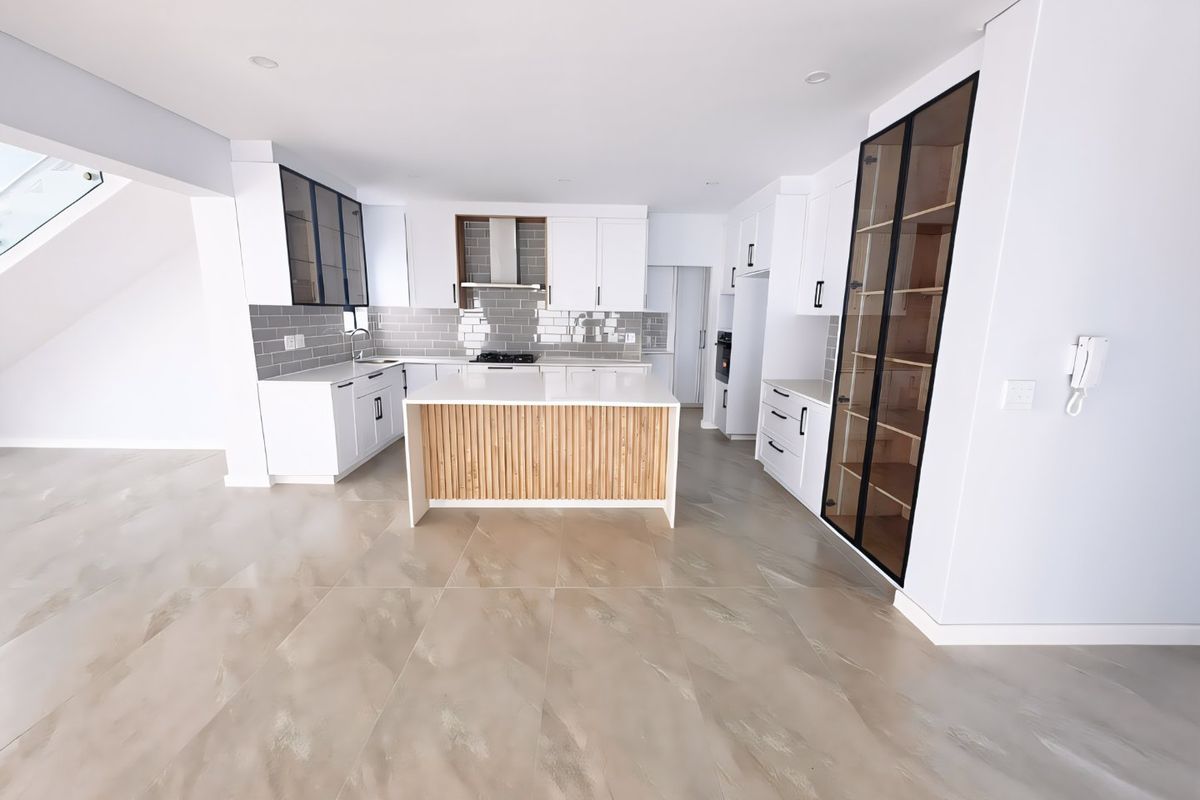 Modern, spacious kitchen featuring a central island with wood-slat detailing, sleek white cabinetry, integrated appliances, and stylish grey subway tile backsplash.
