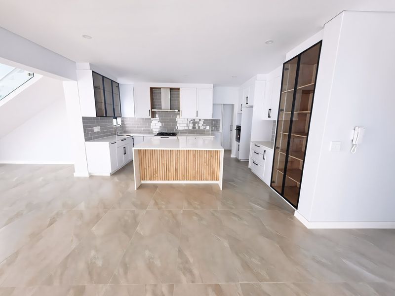 Modern, spacious kitchen featuring a central island with wood-slat detailing, sleek white cabinetry, integrated appliances, and stylish grey subway tile backsplash.