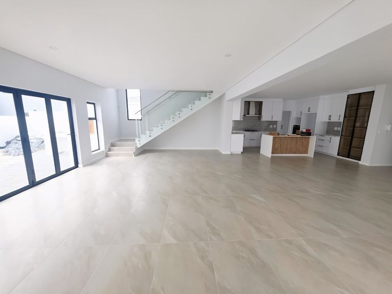 Spacious open-plan living area featuring large format floor tiles, a modern kitchen with island, and a contemporary staircase with glass balustrade.