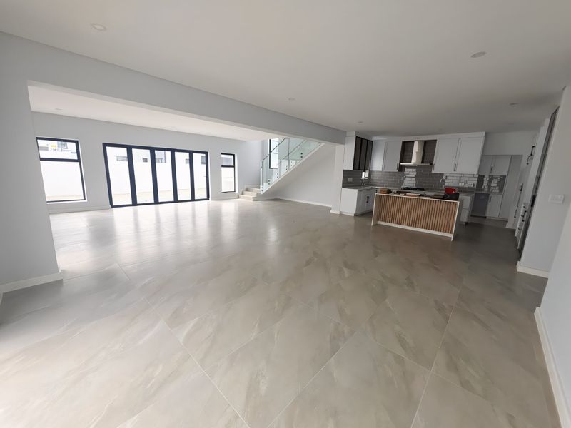 Spacious open-plan living and kitchen area featuring large format floor tiles, modern cabinetry, a kitchen island, and seamless access to the outdoors via bi-fold doors.