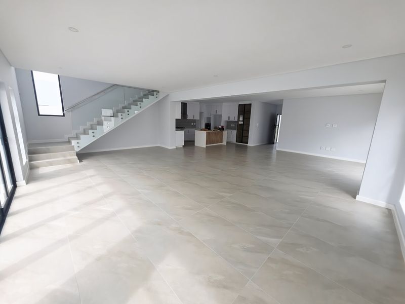 Spacious open-plan living area featuring large format floor tiles, a modern staircase with glass balustrades, and a sleek, contemporary kitchen.