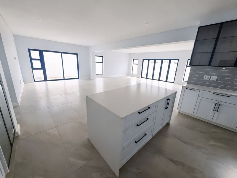 Spacious open-plan living area featuring a modern kitchen island, sleek cabinetry, tiled flooring, and large glass doors providing abundant natural light.