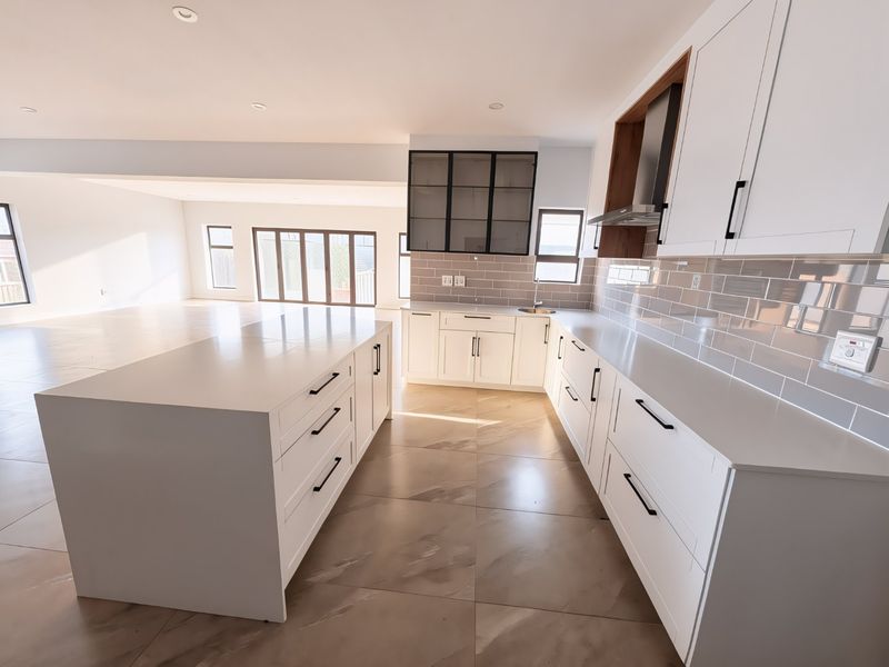 Modern open-plan kitchen featuring a large central island, sleek white cabinetry, subway tile backsplash, and high-quality tiled flooring, flowing into a spacious living area.