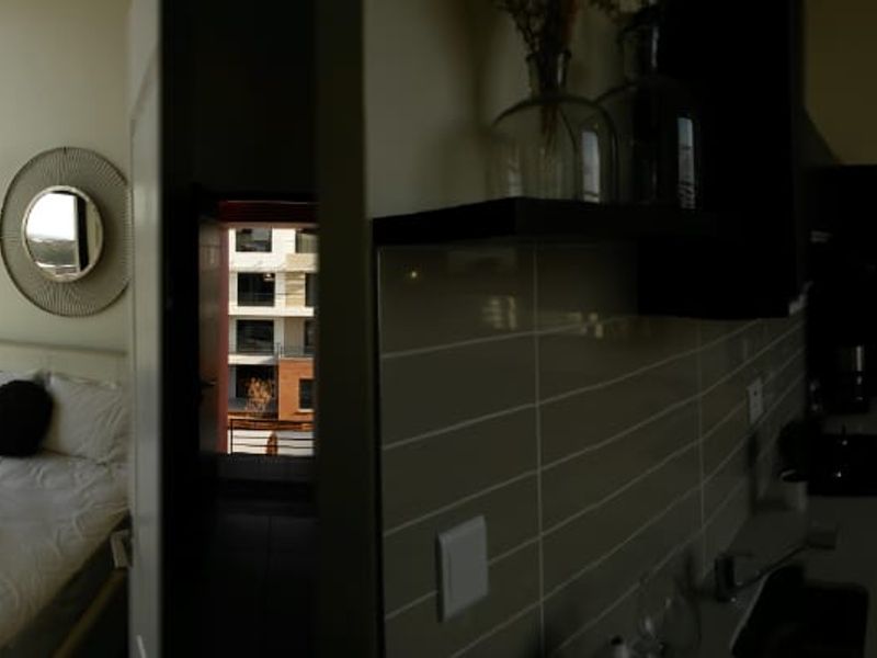 A panoramic view of an open-plan apartment featuring high ceilings, large windows with balcony access, and a modern kitchen area.