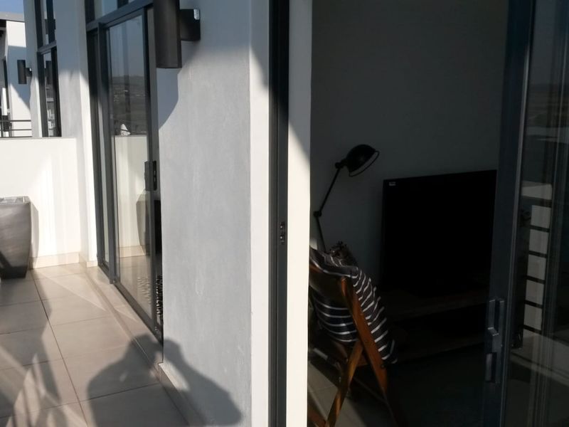 A modern balcony featuring tiled flooring, metal railings, and large sliding glass doors providing seamless access to the interior living space.