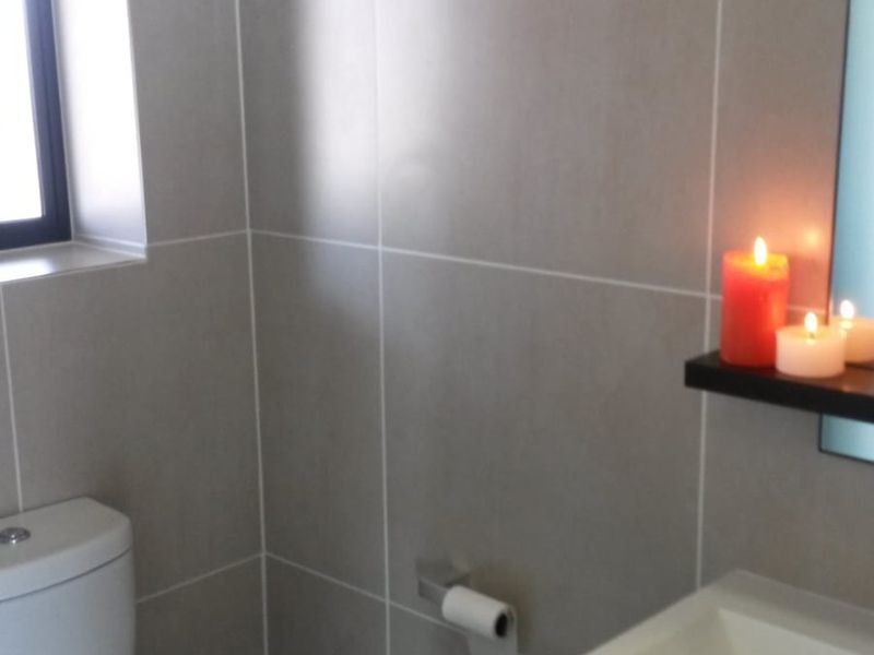 A modern bathroom featuring neutral wall tiles, a sleek vanity with integrated basin, and a toilet.