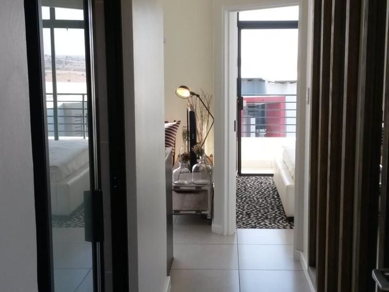 A bright hallway featuring modern tiled flooring, a built-in sliding door cupboard, and decorative timber wall slats leading towards an outdoor balcony area.