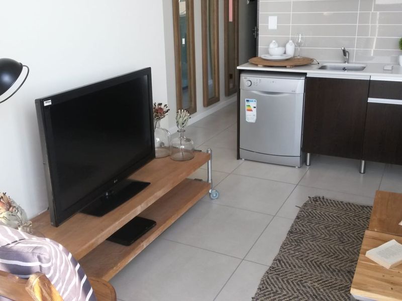 Modern open-plan living area featuring a compact kitchen with built-in cabinetry, stainless steel sink, gas hob, and oven, complemented by neutral tiled flooring.
