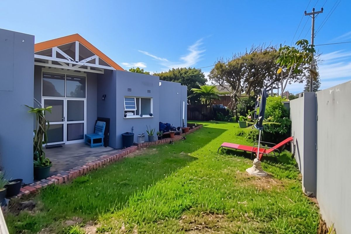 A rear view of the property featuring a paved patio area, a well-maintained lawn, and a secure perimeter boundary wall.