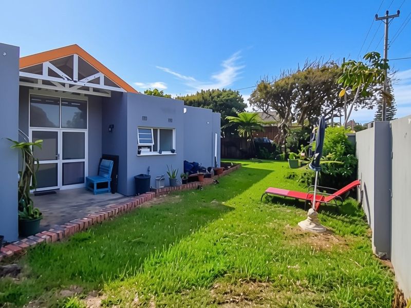A rear view of the property featuring a paved patio area, a well-maintained lawn, and a secure perimeter boundary wall.