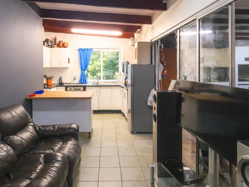 Open-plan living and kitchen area featuring exposed timber ceiling beams, tiled flooring, and functional kitchen cabinetry with a breakfast counter.