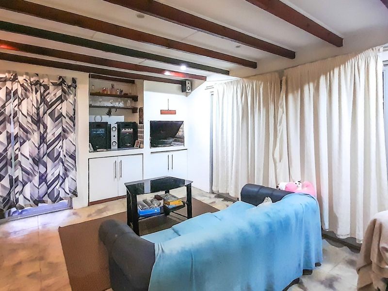 Living room featuring exposed timber ceiling beams, tiled flooring, built-in cabinetry, and sliding glass doors providing access to the exterior.